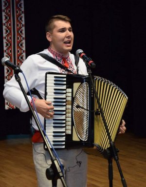 Zdjęcie przedstawia Piotrka Ostaszewskiego śpiewającego, z akordeonem