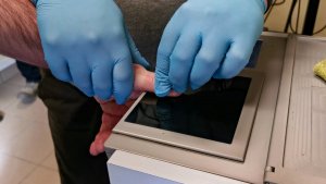 policyjny technik pobiera odciski palców od zatrzymanej osoby