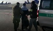 funkcjonariusze na płycie lotniska prowadzą do auta  zatrzymanego mężczyznę. W dali widoczne są samoloty