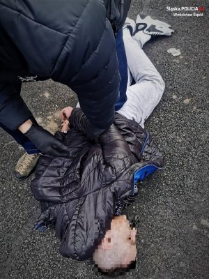 policjant zakuwa zatrzymanego mężczyznę, leżącego na ziemi