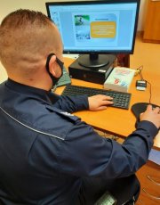 policjant siedzi przed monitorem komputera i prowadzi lekcje on-line z młodzieżą