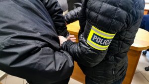 policjant w ubraniach cywilnych zakłada zatrzymanemu kajdanki na ręce trzymane z tyłu&quot;&gt;