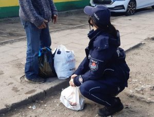 policjantka, która kuca przed stojącym przed nią mężczyzną, trzyma worek