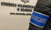 na zdjęciu widoczny jest napis na ścianie: Komenda Wojewódzka w Gdański i fragment adresu www.pomorska.policja. oraz rękaw policjanta, który ma założoną niebieską opaskę z białym napisem: negocjator