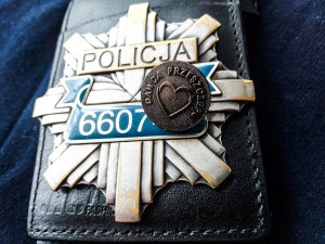 Odznaka policyjna a na niej położone jest metalowe odznaczenie z napisem dawca szpiku