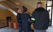 Dwóch nieumundurowanych policjantów prowadzących podejrzanego w budynku Komendy Miejskiej Policji w Piekarach Śląskich