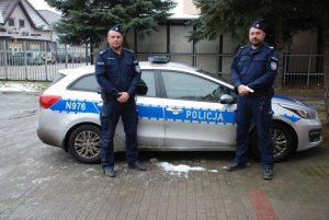 Dwaj umundurowani policjanci stoją przy radiowozie