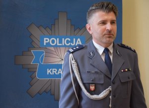 Komendant Miejski Policji w Krakowie mł. insp. Zbigniew Nowak stoi na tle ściany z logiem Policji z Krakowa