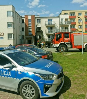 radiowóz policyjny, samochody osobowe i wóz strażacki stojące przed budynkami mieszkalnymi