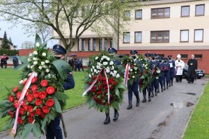 Korowód pogrzebowy, policjanci niosący wiązanki kwiatowe.
