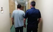 policjant prowadzi korytarzem zatrzymanego mężczyznę