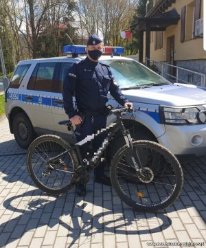 Policjant w mundurze stoi obok radiowozu z rowerem