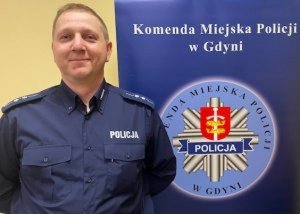 Umundurowany policjant na tle baneru Komendy Miejskiej Policji w Gdyni