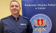 Umundurowany policjant na tle baneru Komendy Miejskiej Policji w Gdyni