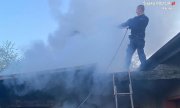 Policjant stojąc na dachu budynku gasi pożar