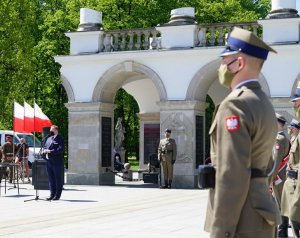 Mężczyzna przed mikrofonem, z boku widoczny żołnierz, z tyłu Grób Nieznanego Żołnierza w Warszawie