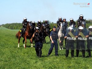 policjanci na koniach, w tle policjanci z oddziałów prewencji z tarczami w ręku stoją na trawie&quot;&gt;