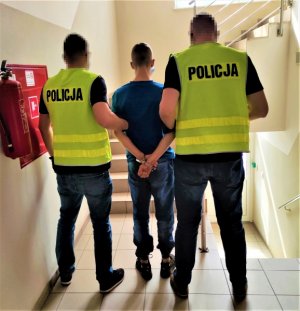 dwaj policjanci w kamizelkach z napisem Policja prowadzą zatrzymanego