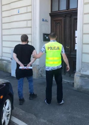 Policjant prowadzi zatrzymanego do budynku prokuratury