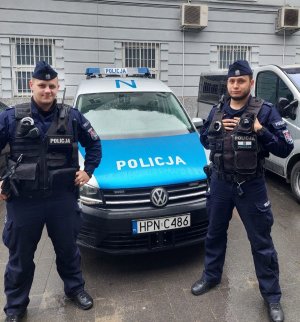 dwaj umundurowani policjanci stoją przy radiowozie