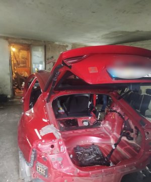 Częściowo zdemontowany samochód osobowy marki KIA koloru czerwonego stojący w garażu