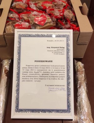 dyplom z podziękowaniami dla policjantów, oparty o karton ze słodyczami