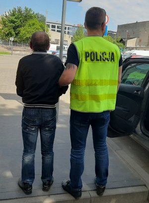 Policjant w żółtej kamizelce z napisem Policja prowadzi zatrzymanego