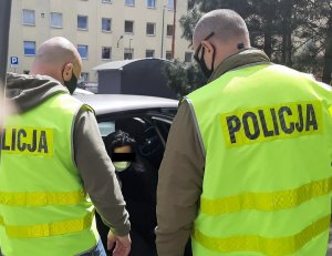 Dwaj policjanci w żółtych kamizelkach z napisem Policja podczas konwojowania zatrzymanej