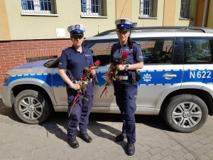 dwie umundurowane policjantki ruchu drogowego przed radiowozem, w ręku trzymają róże