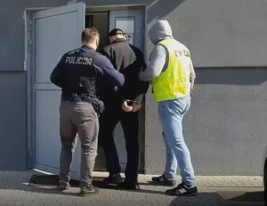 dwaj policjanci wprowadzają zatrzymanego mężczyznę do budynku