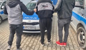 dwaj nieumundurowani policjanci prowadzą zatrzymanego do radiowozu
