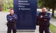 Zdjęcie przedstawia dzielnicowych. Policjanci stoją przy niebieskiej tablicy w napisem Policja, Komenda Powiatowa Policji w Hajnówce