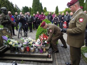 dwaj żołnierze przy grobie, jeden z nich składa kwiaty, w tle uczestnicy rajdu