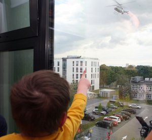 Dziecko pokazujące z okna szpitala na policyjny śmigłowiec podczas lotu.