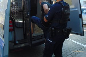 policjant doprowadza zatrzymanego mężczyznę do policyjnego radiowozu