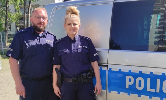 policjant i policjantka stoją przy radiowozie