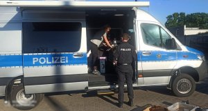 w niemieckim radiowozie stoi osoba, a obok radiowozu stoi umundurowany niemiecki policjant