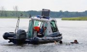policyjna łódź na brzegu której kuca funkcjonariusz, podpływa do dwóch osób znajdujących się w wodzie