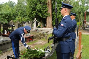 Komendant Główny Policji poprawia wieniec na grobie, z boku widoczni dwaj umundurowani funkcjonariusze którzy pełnią wartę honorową przy grobie