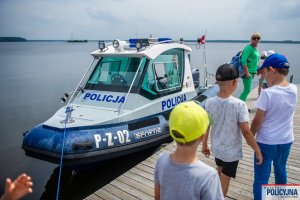Dzieci stojące na pomoście w tle zacumowana łódź Policyjna
