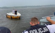 Policjant stoi na łodzi, a za nimi płynie holowana motorówka