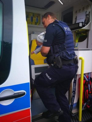 policjant z dzieckiem na ręku wsiada do ambulansu