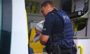 policjant z dzieckiem na ręku podchodzi do ambulansu przy którym stoi ratownik medyczny