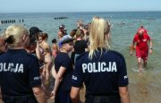 umundurowane policjantki na plaży, nad brzegiem morza, wokół stoją ludzie, a z wody wychodzą ratowncy