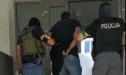 Policjanci wprowadzają do komendy zatrzymanego mężczyznę z kajdankami na rękach z tyłu