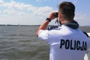 policjant patrzy przez lornetkę stojąc na brzegu jeziora