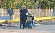Umundurowany policjant pcha wózek inwalidzki z siedzącą na nim kobietą - widok z tyłu