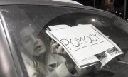 Kobieta z kartka w samochodzie z napisem POMOCY