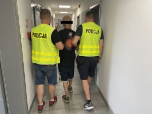 dwaj policjanci praowadzą zatrzymanego mężczyznę korytarzem