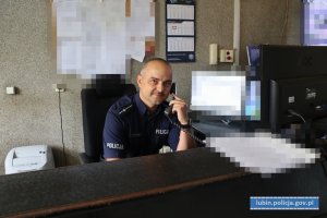 policjant siedzi przy biurku i rozmanwia przez telefon